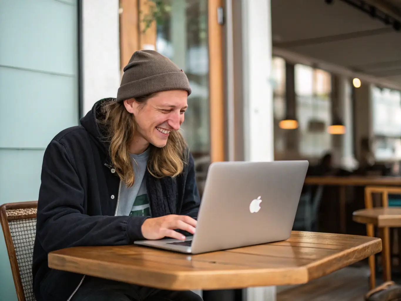 A young woman is smiling while using her laptop at a coffee shop, with a Paygistix personal loan application form visible on the screen. The atmosphere is relaxed and modern, emphasizing convenience and accessibility.